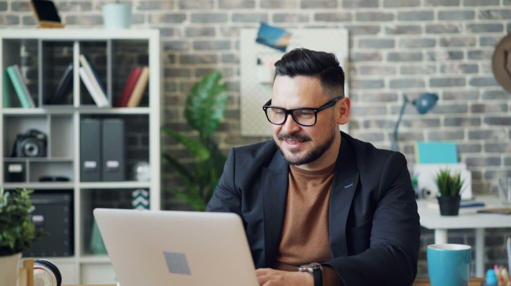 Smiling man working on a laptop at an office desk.
