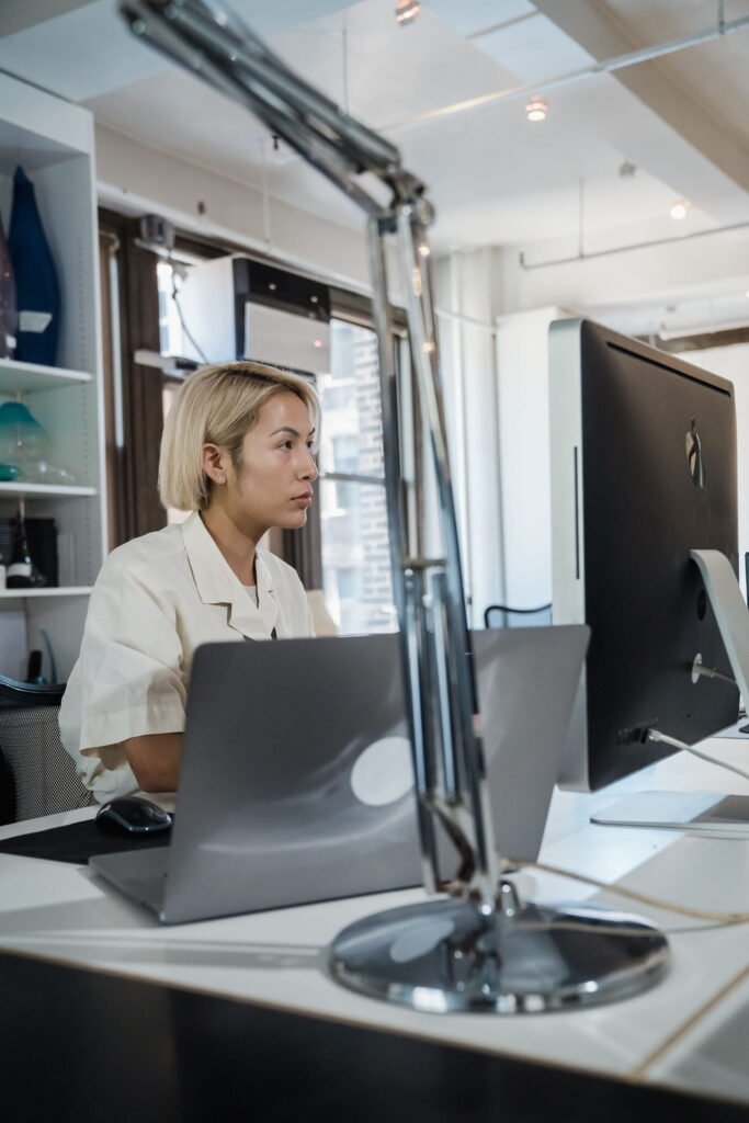 Woman working at a desk with a laptop and external monitor.